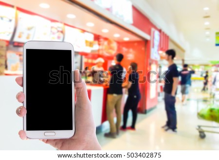 Man use mobile phone, blur image of burgers and ice cream shop as background.