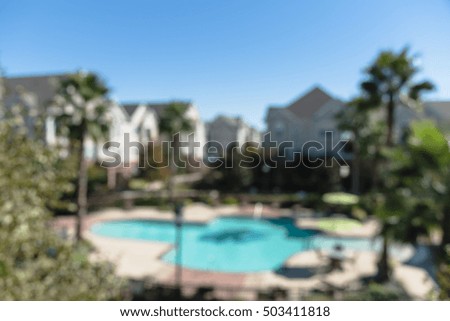 Blurred image outdoor swimming pool and woven rattan pool beds with modern houses in background. Elevated view apartment backyard landscape with swimming pool, palm trees, clear blue sky in Texas, US.
