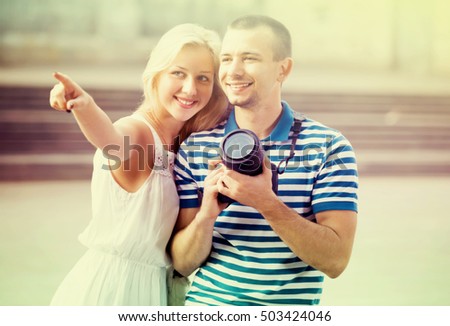 young excited couple looking curious and taking pictures outdoors in trip. Focus on man
