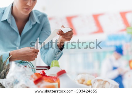 Woman shopping at the supermarket, she is checking a long grocery receipt and leaning on a cart, budgeting and lifestyle concept Royalty-Free Stock Photo #503424655