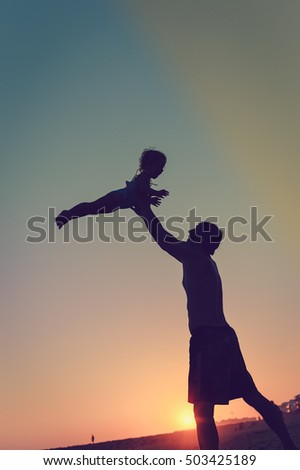 Silhouette of happy family, joyful father throwing up his child in the park on the sunset sky outdoors background