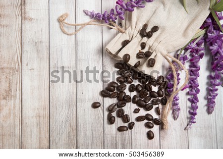 coffee beans in the fabric bag on the wood background with free space on the left and flowers