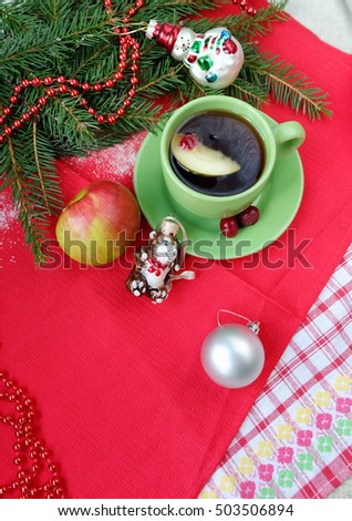Christmas tea. Tea with apples and berries in a green cup and Christmas decorations on the background of Christmas tree branches.
