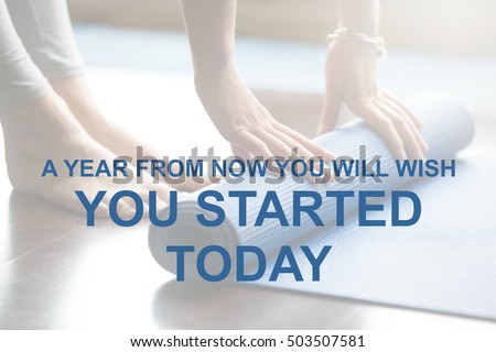 Close-up of attractive young woman folding blue yoga or fitness mat after working out at home. Healthy life, keep fit concepts. Motivational text "A year from now you will wish you started today"