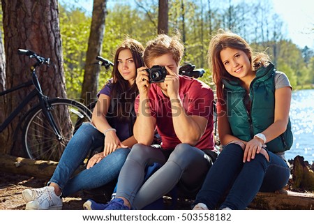 Two girls and a man taking photo pictures on the wild river coast after bicycle ride.