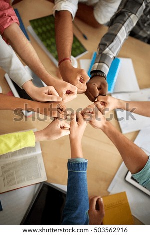 education, school, success, teamwork and people concept - group of international students making fist bump over table