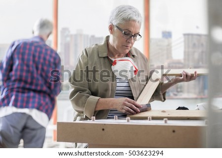 Mature female carpenter sanding picture frame in furniture making workshop