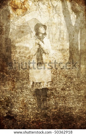 Girl in cloak and scarf with umbrella at park in rainy day. Photo in old image style.