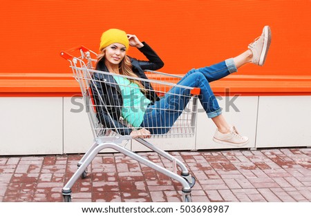 Fashion beautiful woman in trolley cart wearing black jacket hat over colorful orange background