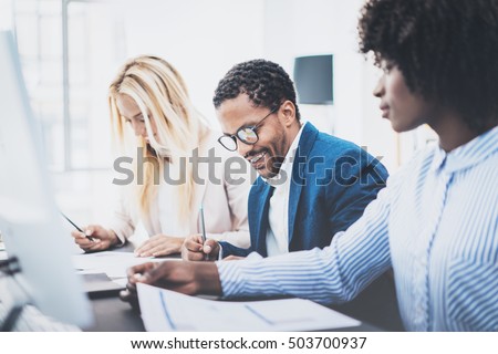 Three young coworkers working together in a modern office.Man wearing glasses and making notes with colleague on documents.Horizontal,blurred background.