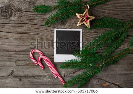 Christmas wooden background with photo frame, red star, candy cane and snow fir tree. Top view with copy space. Holiday concept.