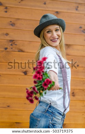 Beautiful blonde modern hipster girl with hat gives flowers to the camera