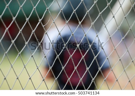 Baseball player out of focus behind baseball cage net. Royalty-Free Stock Photo #503741134