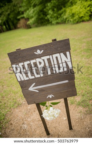 Wedding reception sign made out of wood with paint and and arrow with flowers hanging below.
