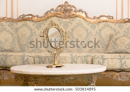 Royal golden frame on table in vintage interior. Closeup of mirror represented on table in royal apartment. Royalty concept.