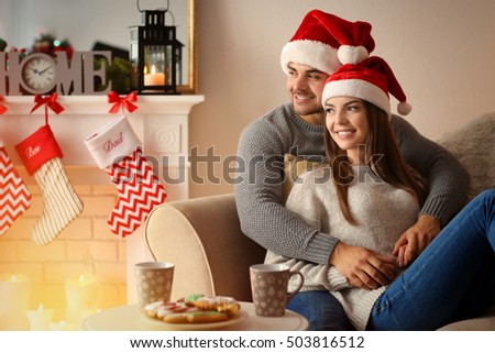 Young couple in Santa Claus hats resting at home