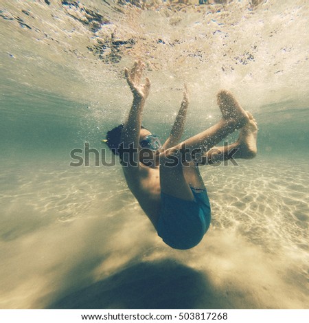 Young boy wearing snorkel mask falling underneath water. 