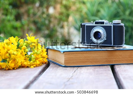 old book, vintage photo camera next to field flowers on wooden table outdoors at afternoon. selective focus