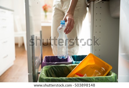 Man putting empty plastic bottle in recycling bin in the kitchen. Person in the house kitchen separating waste. Different trash can with colorful garbage bags.  Royalty-Free Stock Photo #503898148