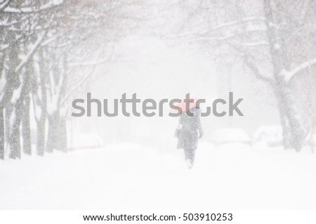 Silhouette of a woman in a dark coat with a red umbrella in a snow storm. Soft focus, blurred outlines. Street of the city in the winter blizzard and snow with beautiful snow flakes.