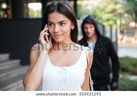 Beautiful young woman talking on mobile phone and being stalked by man criminal on the street Royalty-Free Stock Photo #503921293