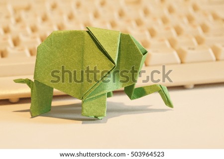 Paper origami elephant isolated on white background on the table next to the computer keyboard