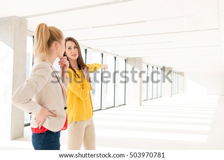 Young businesswoman discussing with female colleague in empty office