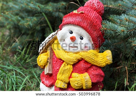 Snowman toy on the grass under the spruce, the celebration of Christmas in a warmer climate