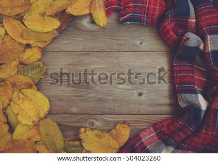 Flat lay view of autumn leaves and tartan textured scarf on wooden background 