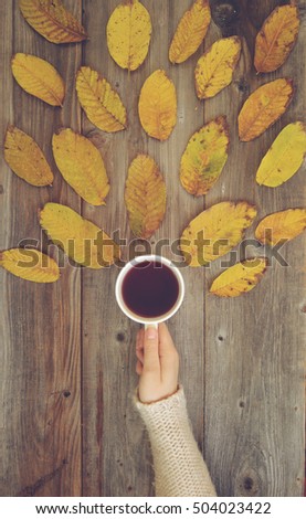 Flat lay view of woman drinking hot drink in cup on wooden desk with autumn leaves