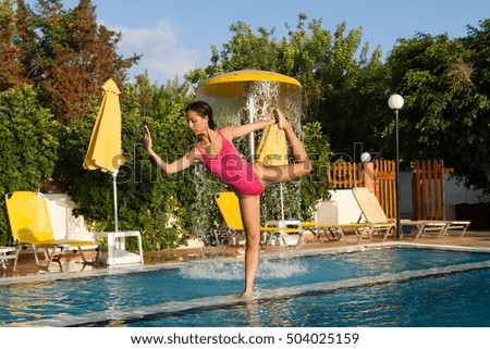 Brunette longhaired woman performs yoga workout by the pool.