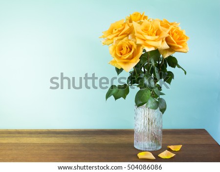 Yellow roses in a retro glass vase on wood table