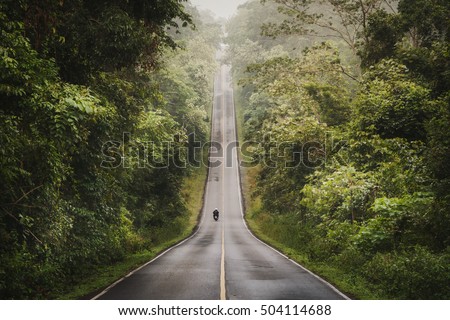 Biker is riding a motorcycle on the road ascending to the top of the hill. Location: Khao Yai National Park, Thailand. Dong Phayayen-Khao Yai Forest Complex Royalty-Free Stock Photo #504114688