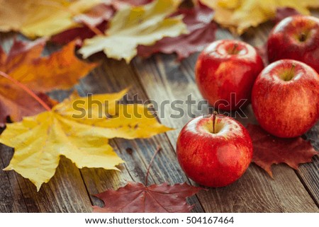 Red autumn apples with fallen leaves on wooden table