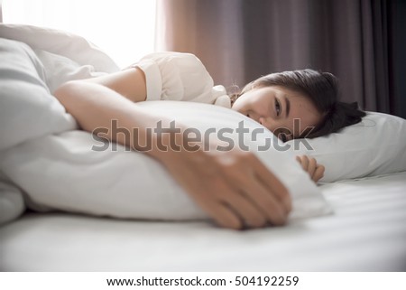 Cute girl on a soft white bed. She woke up from sleep all night . Shows the gentle eyes of a person next. Show a lifestyle of a girl on relaxing morning in holiday. Royalty-Free Stock Photo #504192259