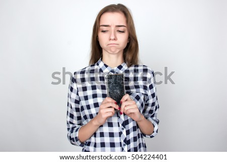 Portrait of a pretty sad woman  in plaid shirt holding smartphone with broken screen standing over gray background and looking at left side