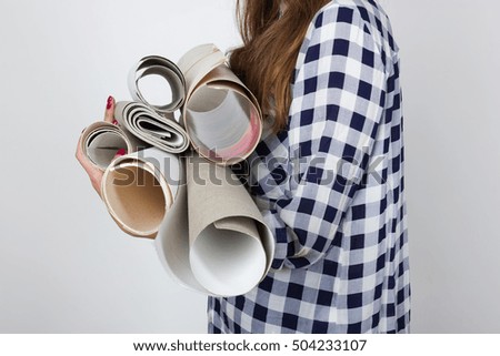 Portrait of a pretty woman  in plaid shirt holds drawings in rolls  standing over gray background 
