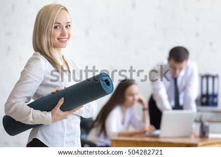 Business and healthy lifestyle concept. Beautiful sporty young office woman finished her work and going at fitness training. Cheerful model posing with exercise mat and friendly smiling at camera Royalty-Free Stock Photo #504282721