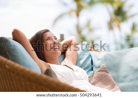 Home lifestyle woman relaxing enjoying luxury sofa patio furniture on outdoor patio living room. Happy lady lying down on comfortable pillows daydreaming thinking. Beautiful young Asian chinese girl. Royalty-Free Stock Photo #504293641