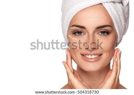 Beauty smiling Girl with towel on head applies cream on face, isolated on white. Concept of healthcare, beauty and youth. Close up photo of Beautiful woman with hand near face. Drops cream around eyes