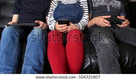 Three children playing with electronic devices - tablet, smartphone and games controller Royalty-Free Stock Photo #504325807