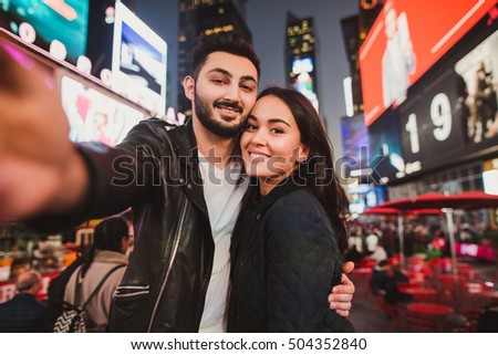 Beautiful multiracial couple in love taking selfie photo for blog on Times Square in New York while travel across USA