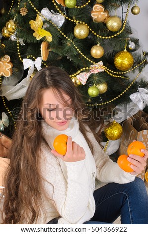 beautiful girl sitting under Christmas tree and holding mandarin orange