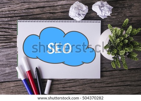 Notepad and green plant on wooden background with SEO word