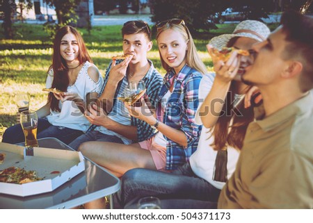 Cheerful friends on picnic in the park. Eating pizza.