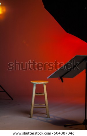 Red Colored Empty Photo Studio Background. Wooden Stool And Softbox. Beauty Lighting. Selective Focus Blurry Background.