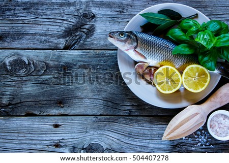 Raw fish with lemon, herbs and spices for cooking on grunge wooden background, top view