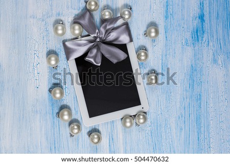 tablet with silver ribbon gift on white cracked blue background, concept of holiday gift