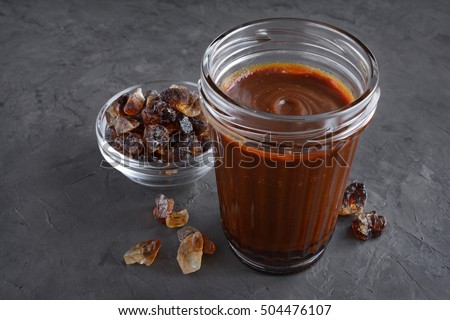 Caramel and caramelized sugar in glass bowl on black concrete background