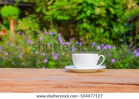 a selective focus picture of a cup of coffee on wooden table in green garden 
